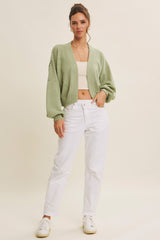 woman wearing a light green oversized cardigan with balloon sleeves and white high waisted jeans, standing against a neutral background