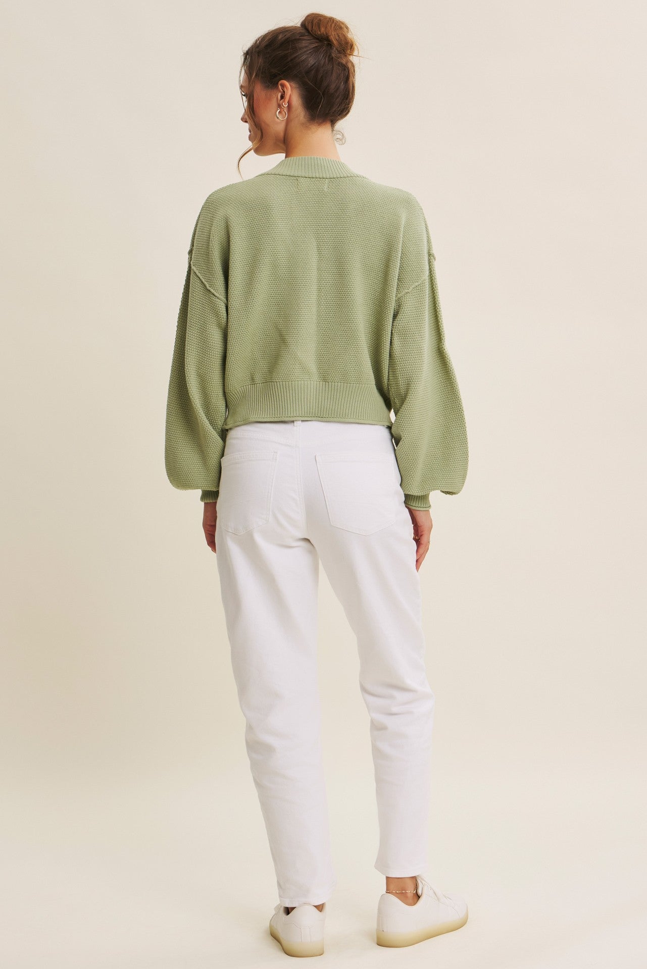 woman wearing a green oversized knit sweater and white high-waisted jeans, seen from the back