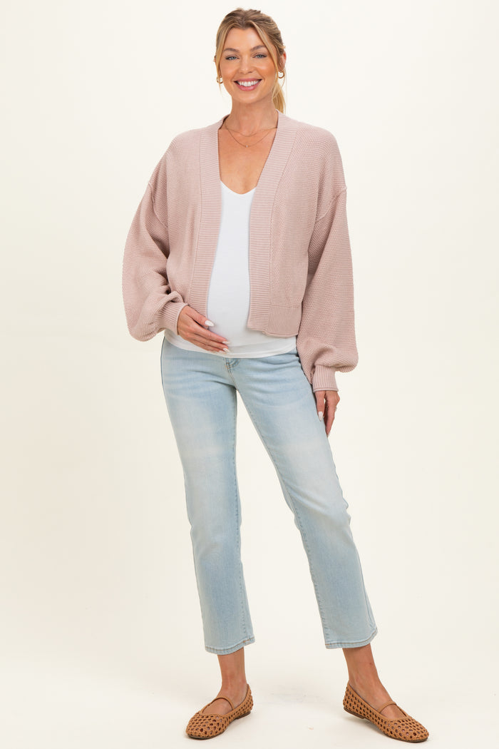 woman wearing a light pink maternity cardigan over a white top and showing her baby bump, paired with light wash jeans