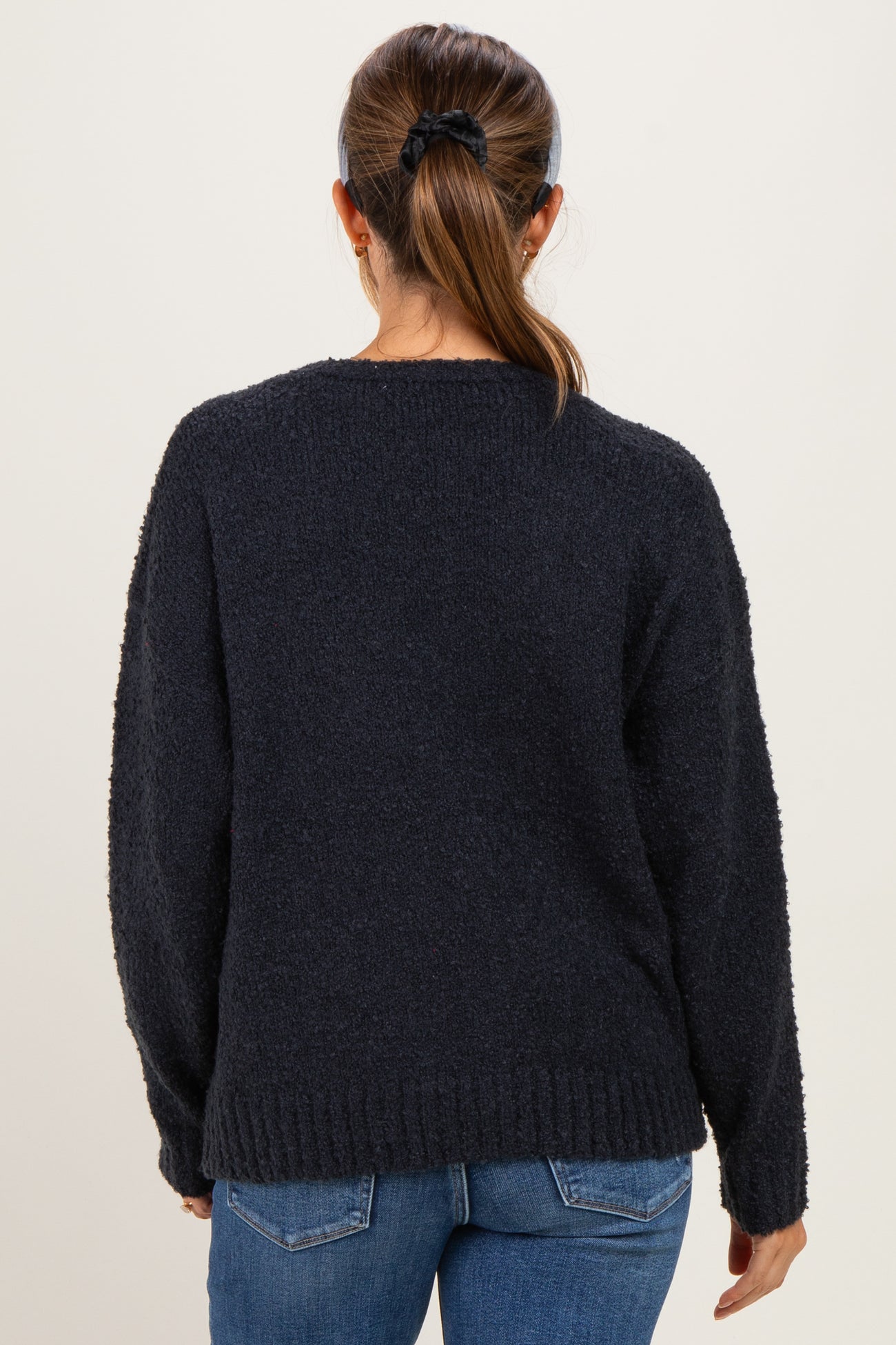 woman wearing a dark grey maternity sweater with a relaxed fit and long sleeves, styled with blue jeans