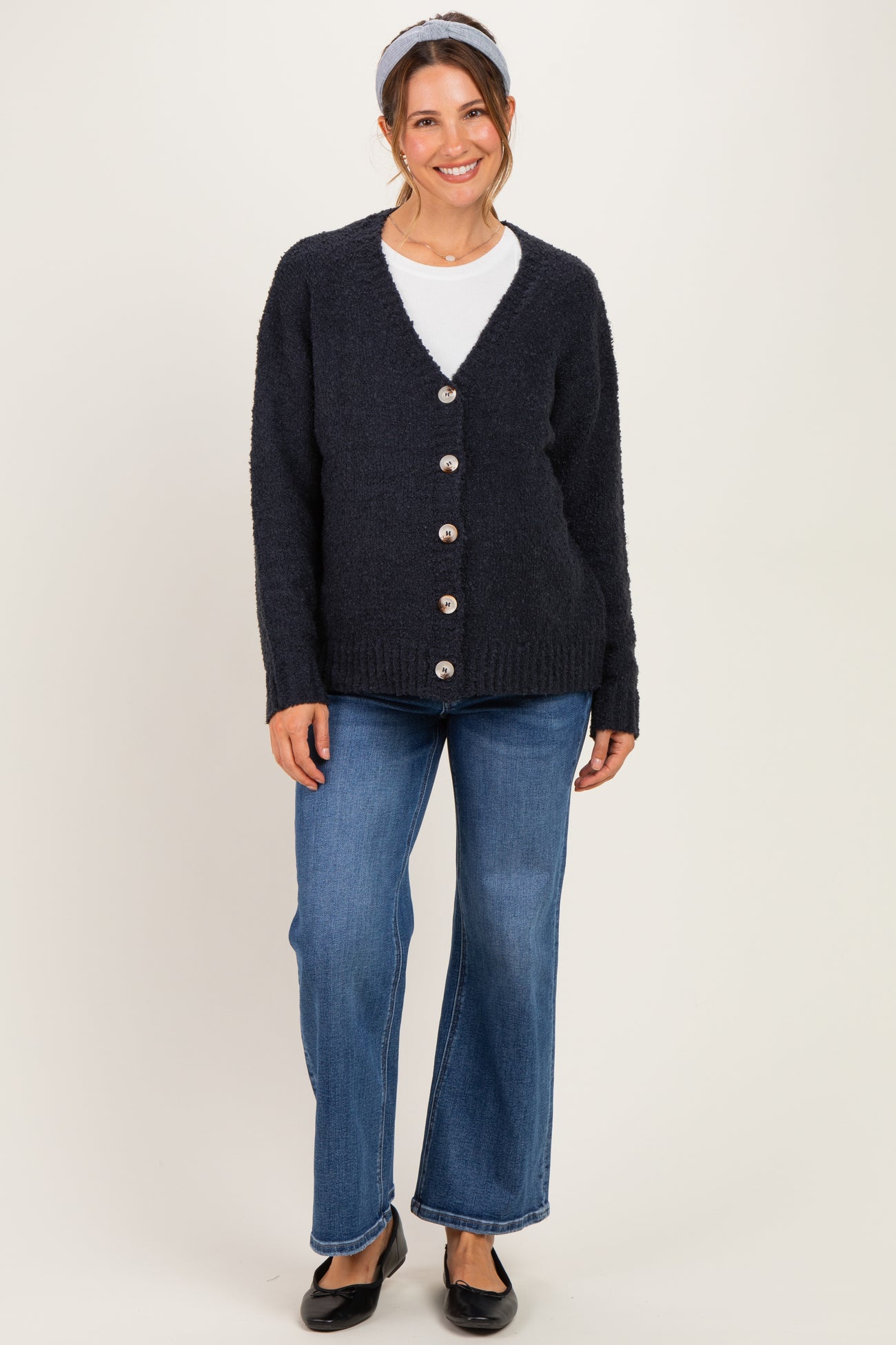 woman wearing a navy blue fuzzy maternity cardigan with buttons and paired with flared denim jeans