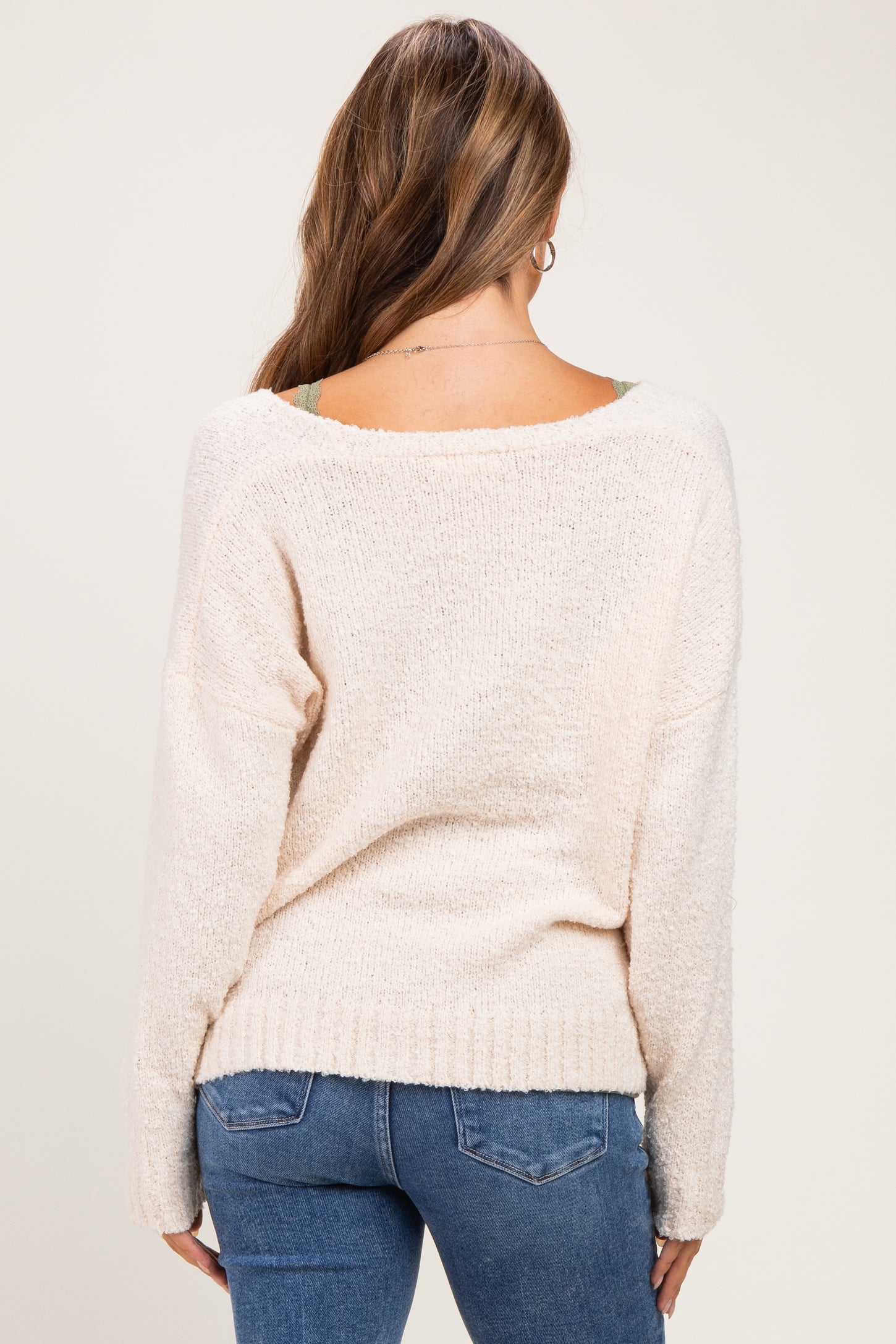 woman wearing a cozy cream maternity sweater with a relaxed fit and open back, shown from the back
