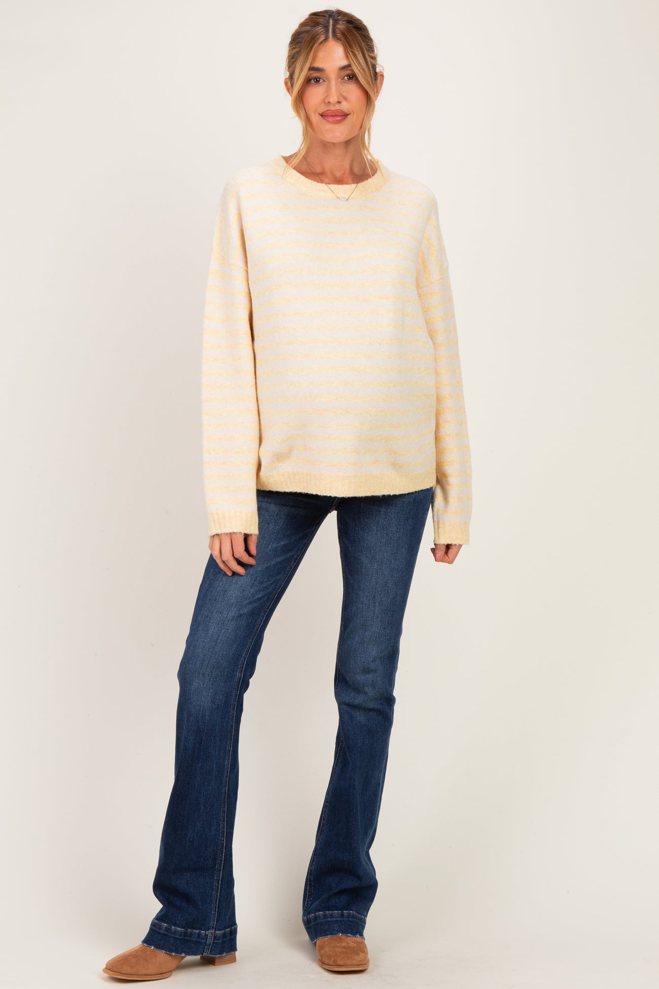 woman wearing a striped yellow maternity sweater with relaxed fit and blue flared jeans