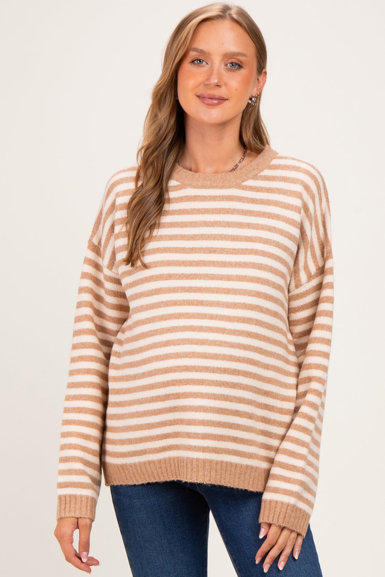 woman wearing a tan and cream striped maternity sweater with a relaxed fit and a rounded neckline