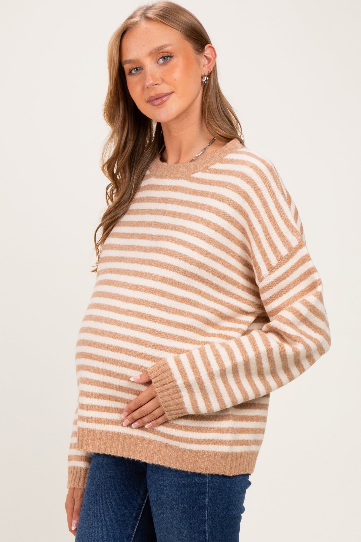 woman wearing a tan and white striped maternity sweater and gently touching her baby bump