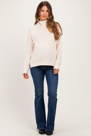 woman wearing a light pink maternity sweater and blue flared jeans, with a baby bump visible