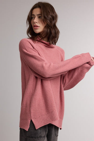 woman wearing a pink oversized sweater with a hood and side slits, styled with casual gray pants