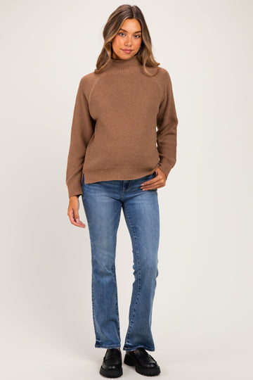 woman wearing a brown maternity sweater with a mock neck and blue flared jeans, no baby bump visible
