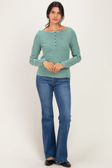 woman wearing a green and white striped long sleeve top with buttons and blue flared jeans