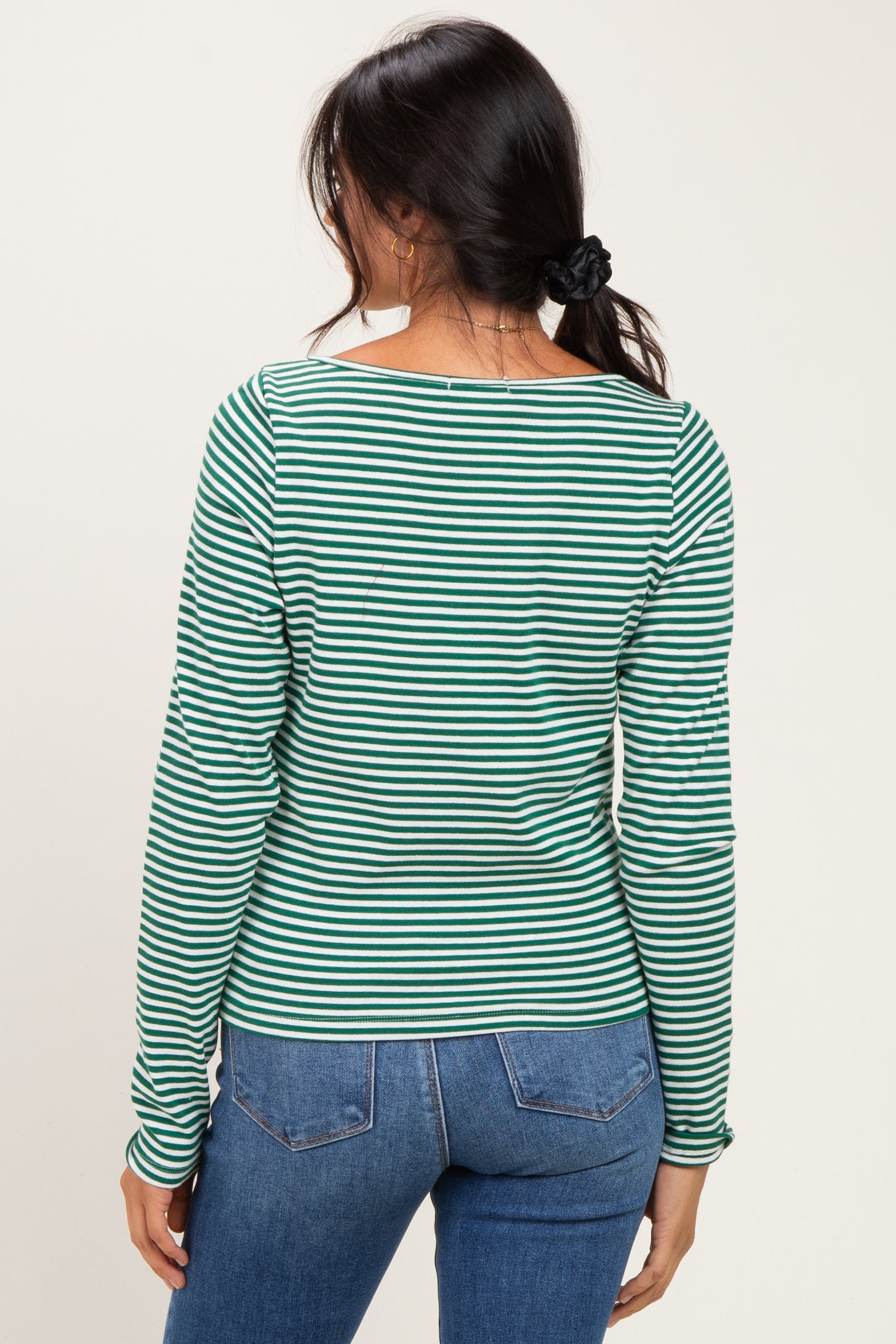 woman wearing a green and white striped long sleeve top, viewed from the back, paired with blue jeans