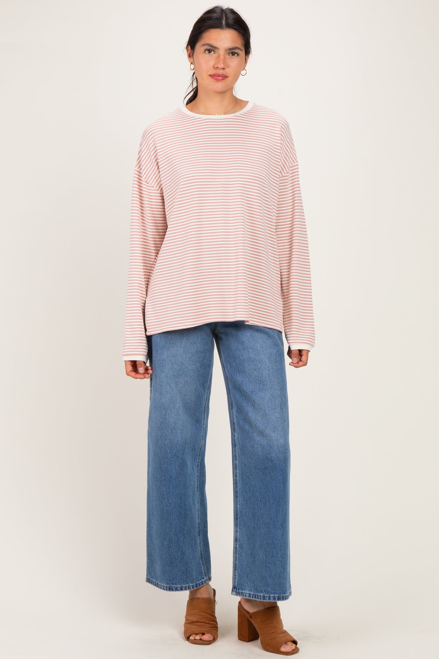 woman wearing a light pink and white striped oversized long sleeve top with blue wide leg jeans and brown heeled mules
