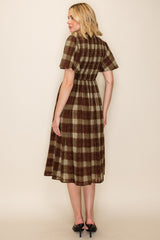 woman wearing a brown and green plaid midi dress with short sleeves, showing the back view and gathered waist detail