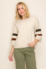woman wearing a cream oversized sweater with green and brown striped sleeves and olive green pants