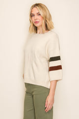 woman wearing an ivory oversized sweater with color block stripes on the sleeves and green trousers