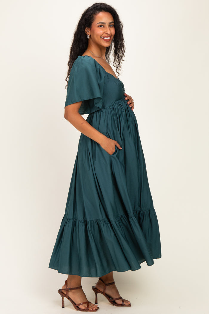 woman wearing a dark green maternity maxi dress with short flutter sleeves and pockets, showing baby bump