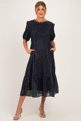 woman wearing a navy blue floral maternity dress with puff sleeves and pockets, showcasing her baby bump
