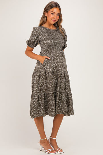 woman wearing a dark floral print maternity dress with puff sleeves and pockets, showing her baby bump