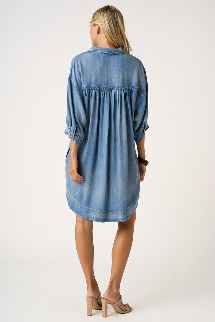 woman wearing a loose-fitting light blue denim dress with three-quarter sleeves and a gathered back detail