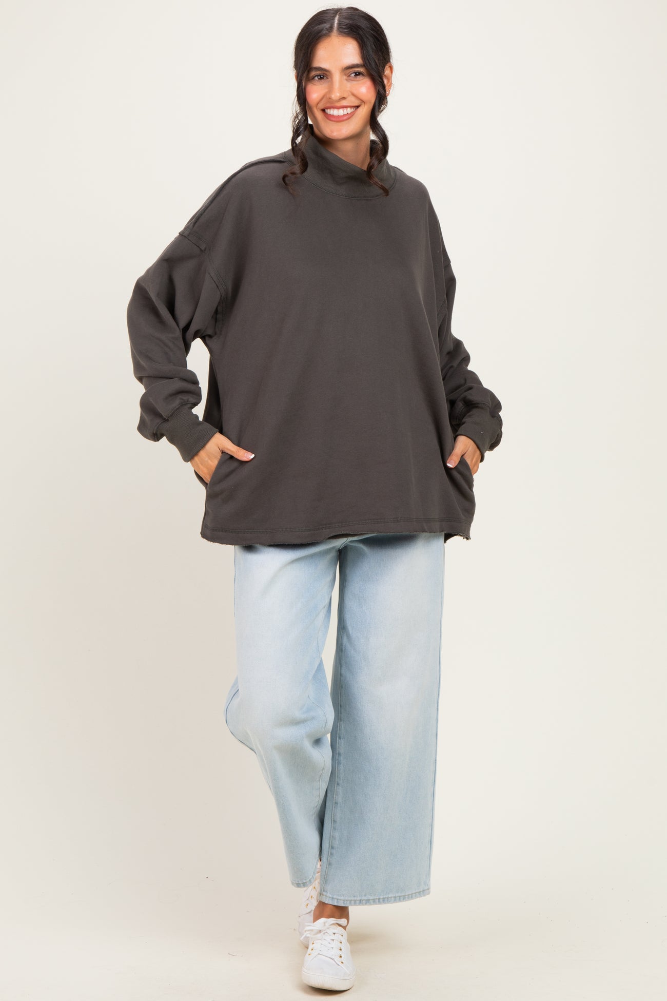 woman wearing an oversized dark gray sweatshirt with side pockets and light blue wide-leg jeans