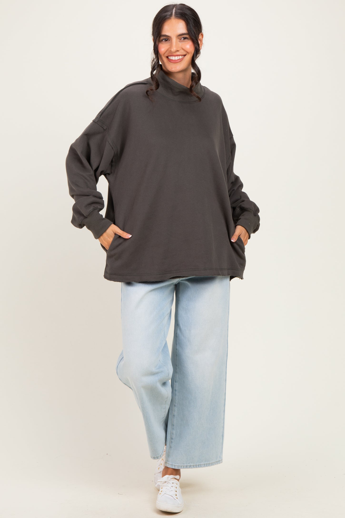 woman wearing an oversized dark gray sweatshirt with side pockets and light blue wide-leg jeans