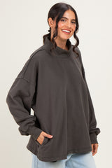 woman wearing an oversized dark gray turtleneck sweatshirt with side pockets and relaxed sleeves