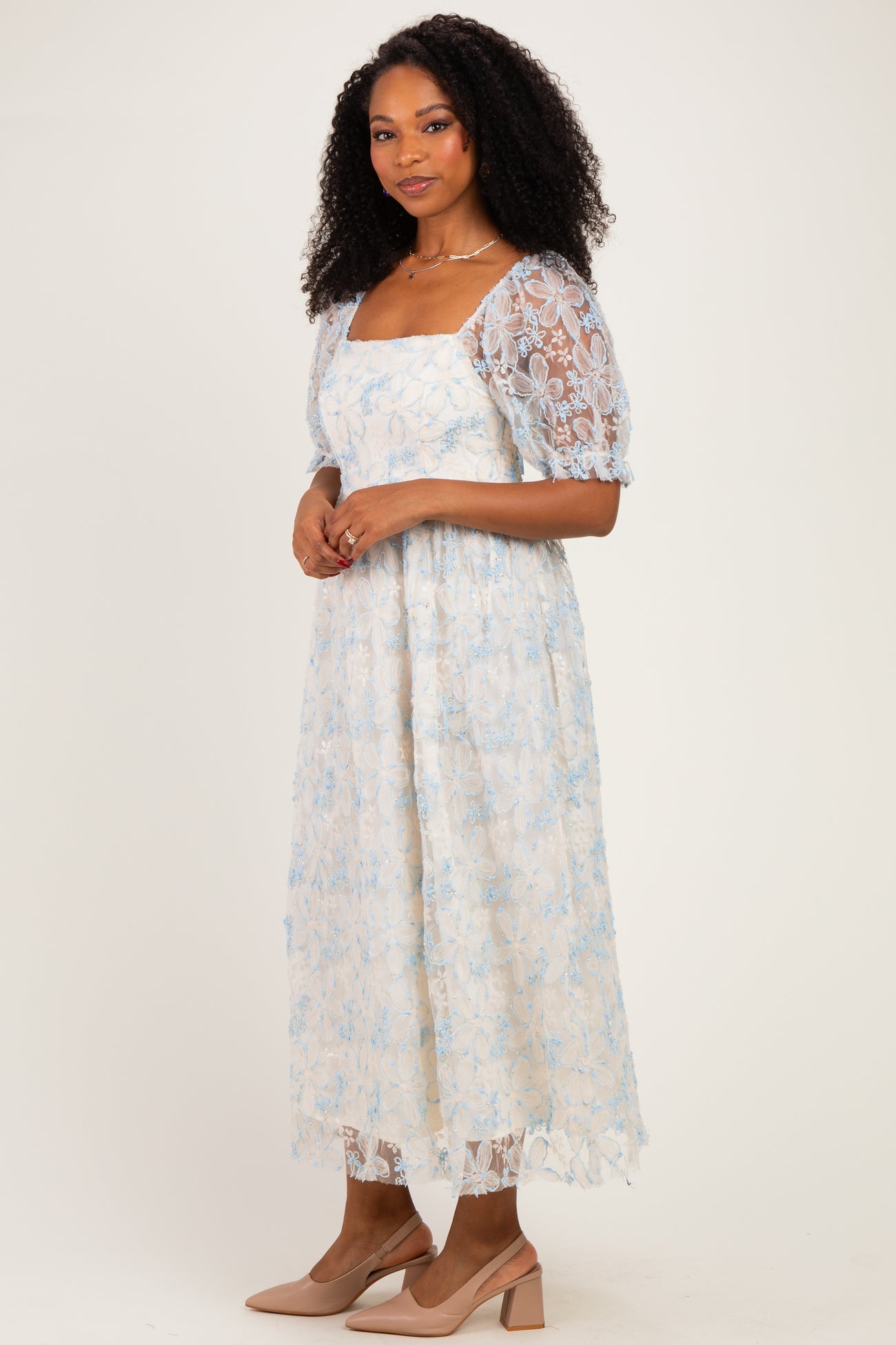 woman wearing a light blue floral lace midi dress with puff sleeves and nude high-heeled shoes
