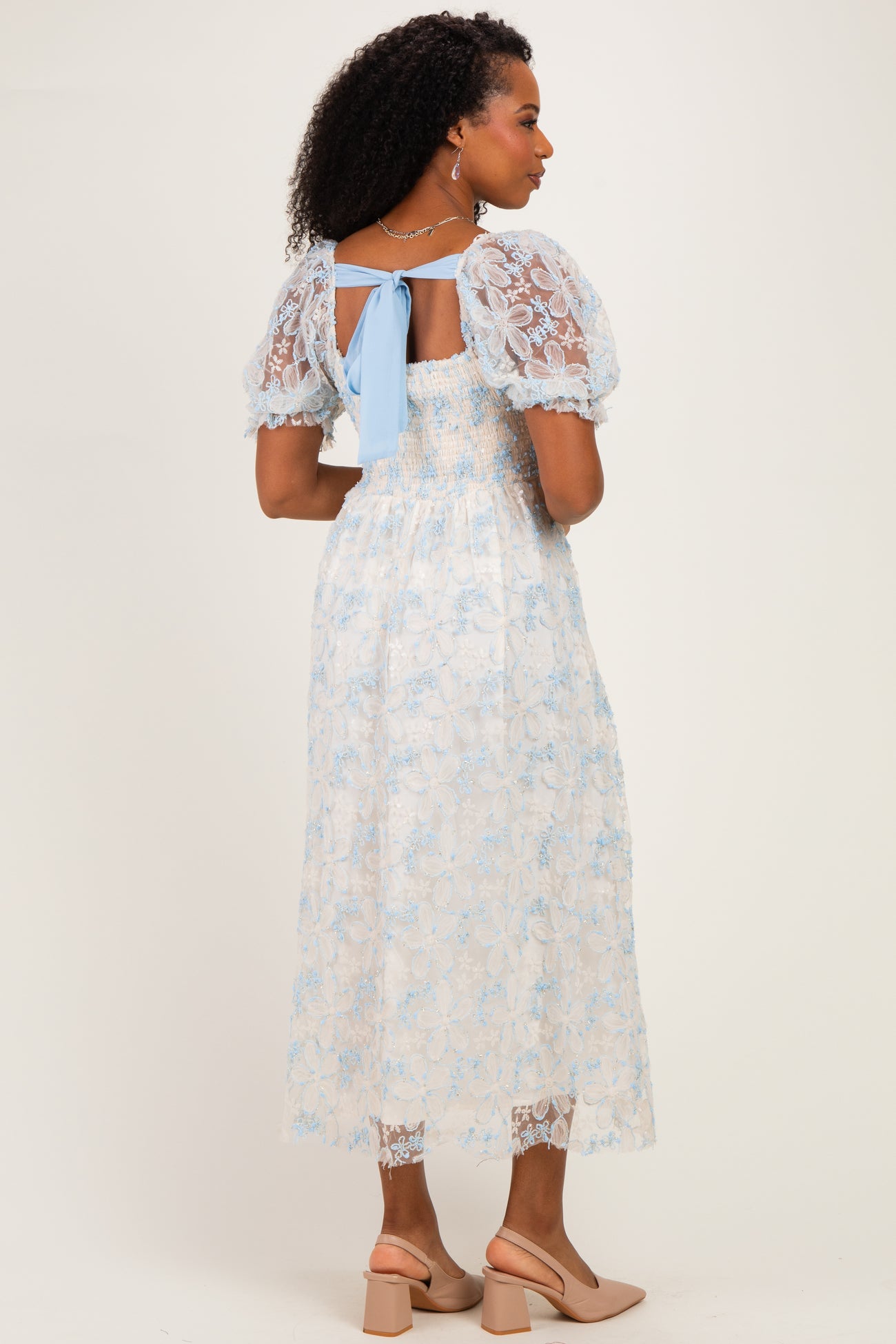woman wearing a light blue floral lace midi dress with puff sleeves and a back tie detail