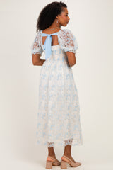 woman wearing a light blue floral lace midi dress with puff sleeves and a back tie detail