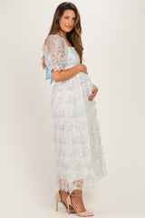 woman wearing a light blue lace maternity dress with a ribbon detail, holding her baby bump