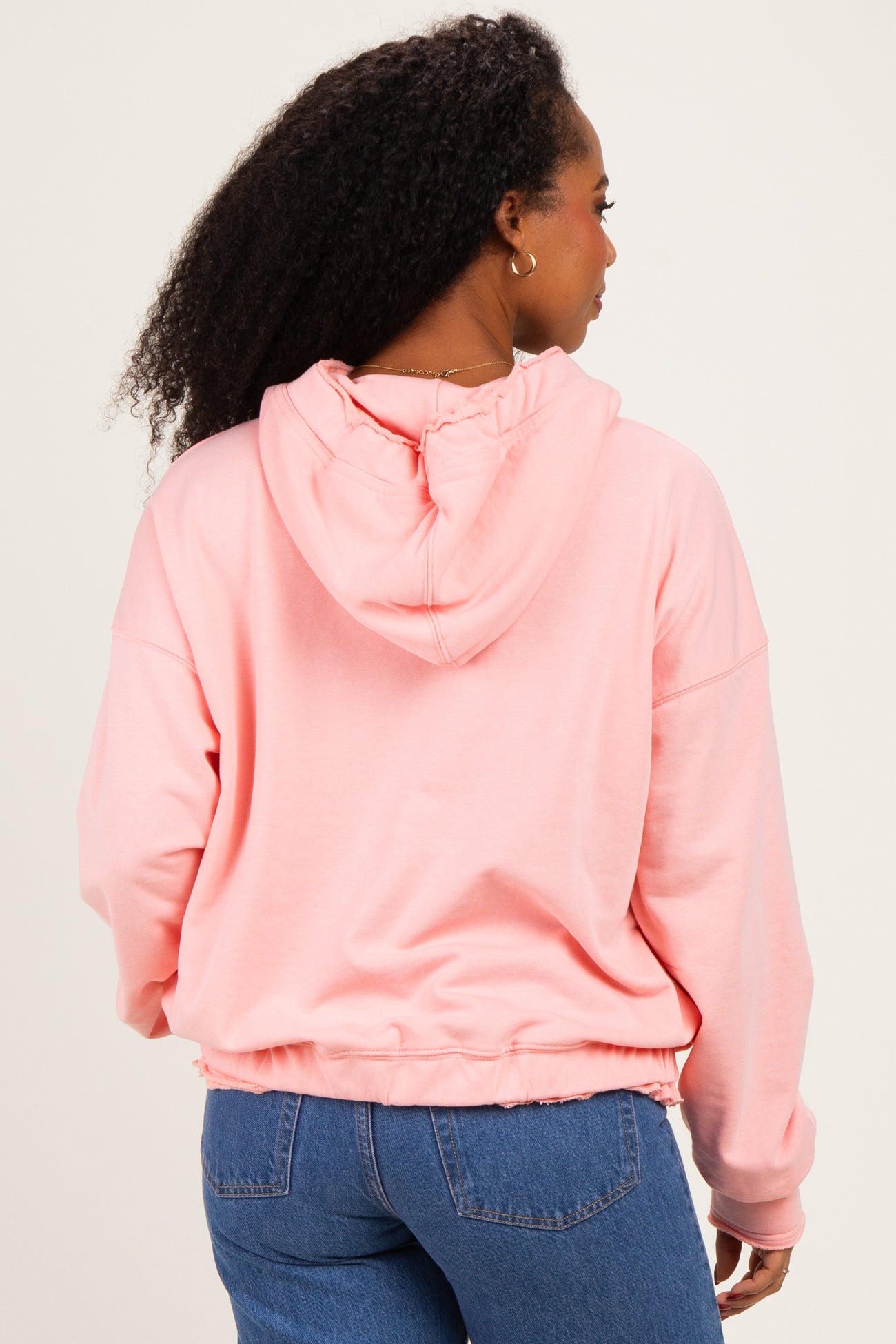 woman wearing a pink cropped hoodie with a drawstring hood and back seam detail, paired with blue jeans