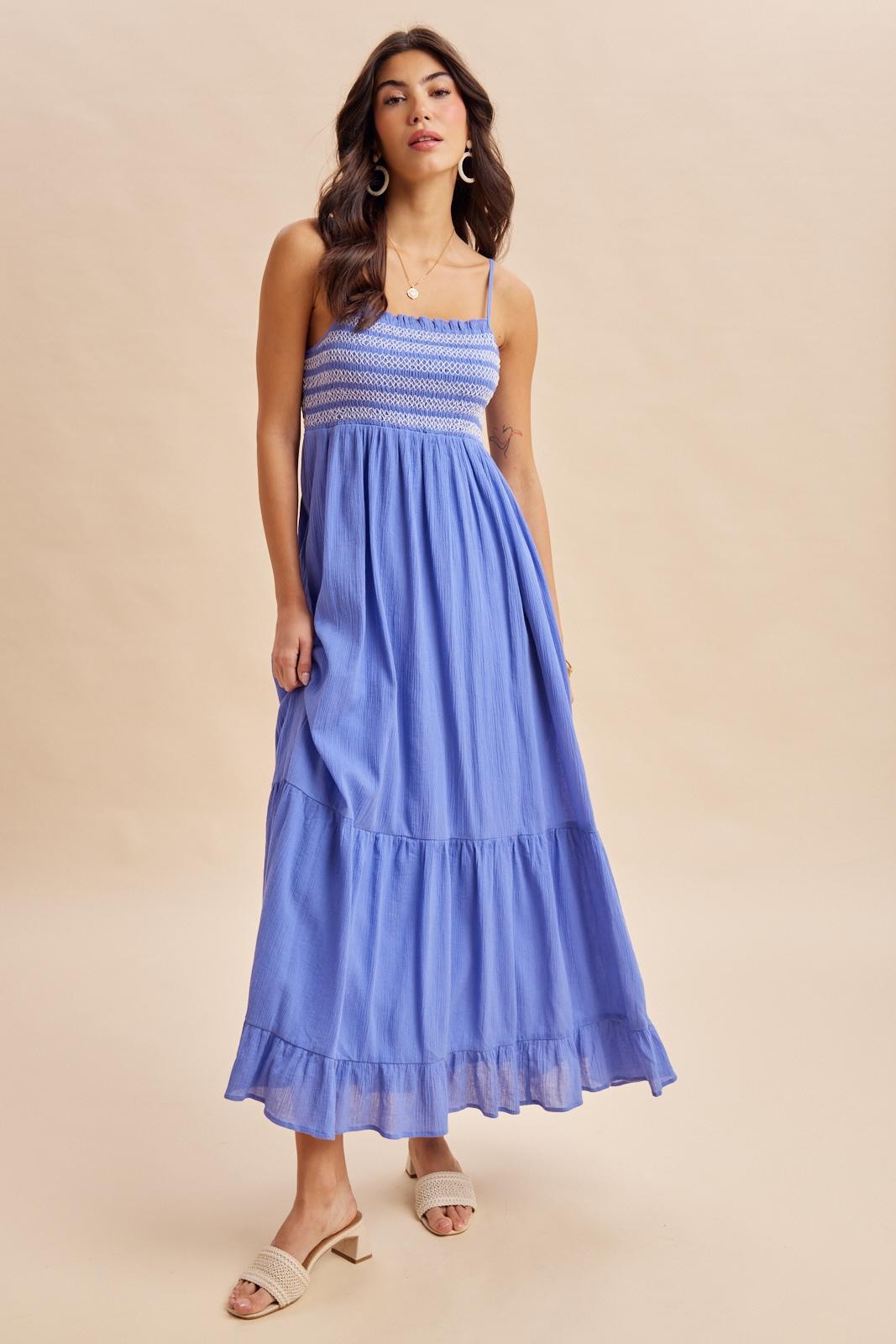 woman wearing a blue maxi dress with a smocked bodice and ruffled hem, standing on a neutral background
