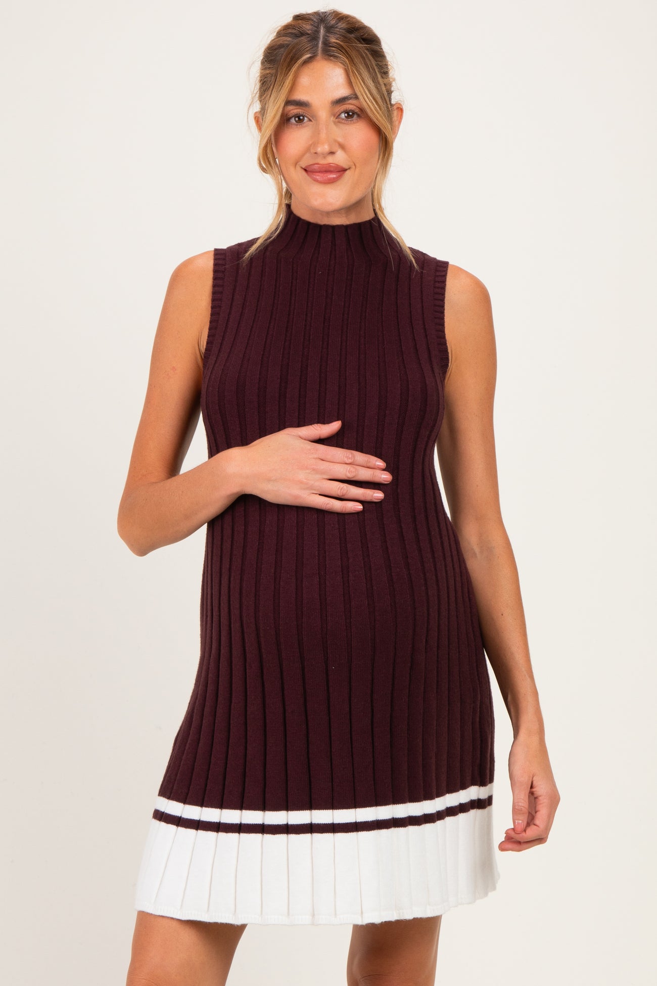 woman wearing a burgundy ribbed maternity dress with a sleeveless design and pleated white skirt, showing her baby bump