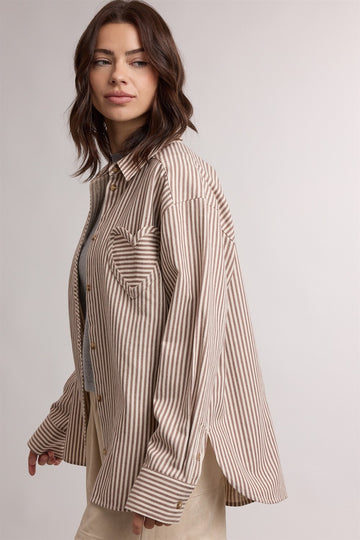 woman wearing a beige and white striped oversized button-up shirt styled casually with a gray top underneath
