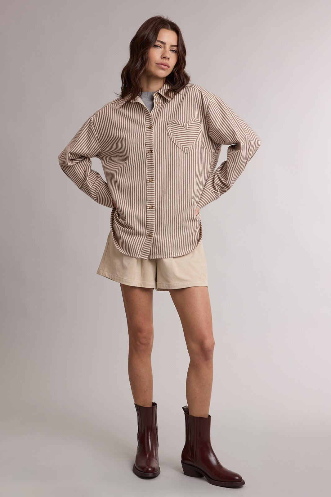 woman wearing a brown and cream striped oversized shirt with a pocket, paired with beige shorts and brown ankle boots