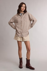 woman wearing a brown and cream striped oversized shirt with a pocket, paired with beige shorts and brown ankle boots