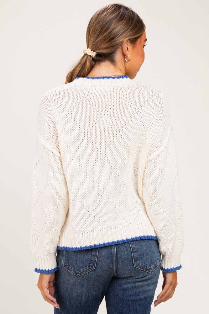 woman wearing a cream-colored knitted maternity sweater with blue trim, showing the back view and relaxed fit