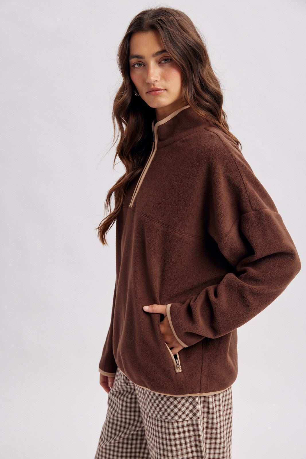 woman wearing a brown zip-up fleece pullover with a high neck and contrasting trim, paired with checked pants