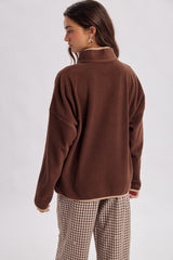woman wearing a brown fleece pullover with a high collar and oversized fit, paired with checkered trousers