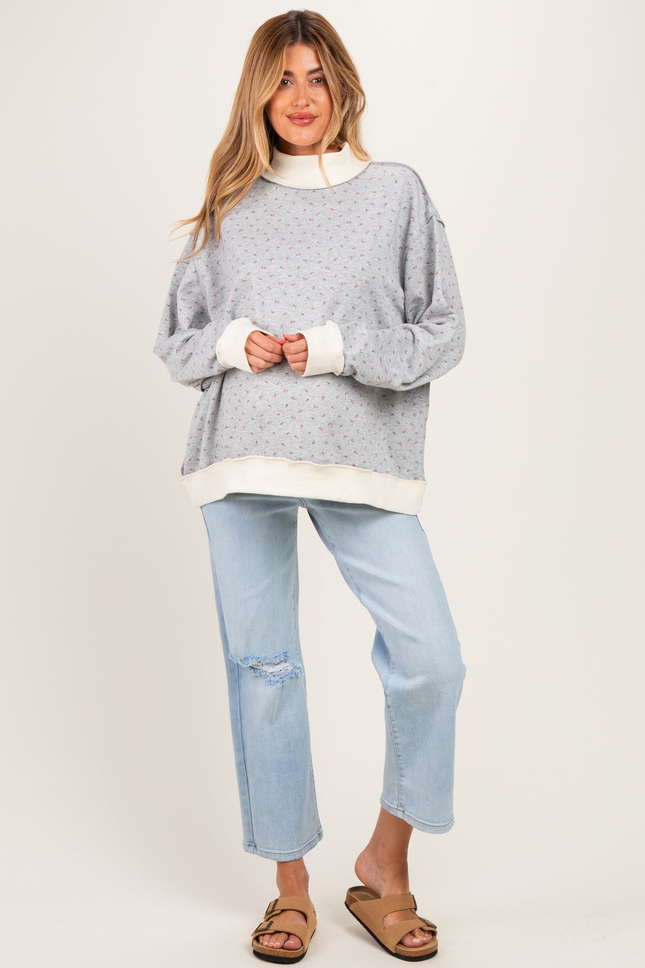 woman wearing a gray maternity sweatshirt with floral pattern and white accents, paired with light blue distressed jeans