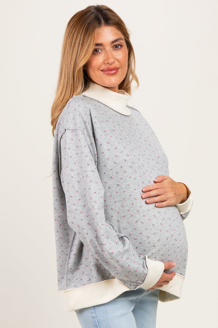 woman wearing a gray floral maternity sweatshirt with a white collar and holding her baby bump