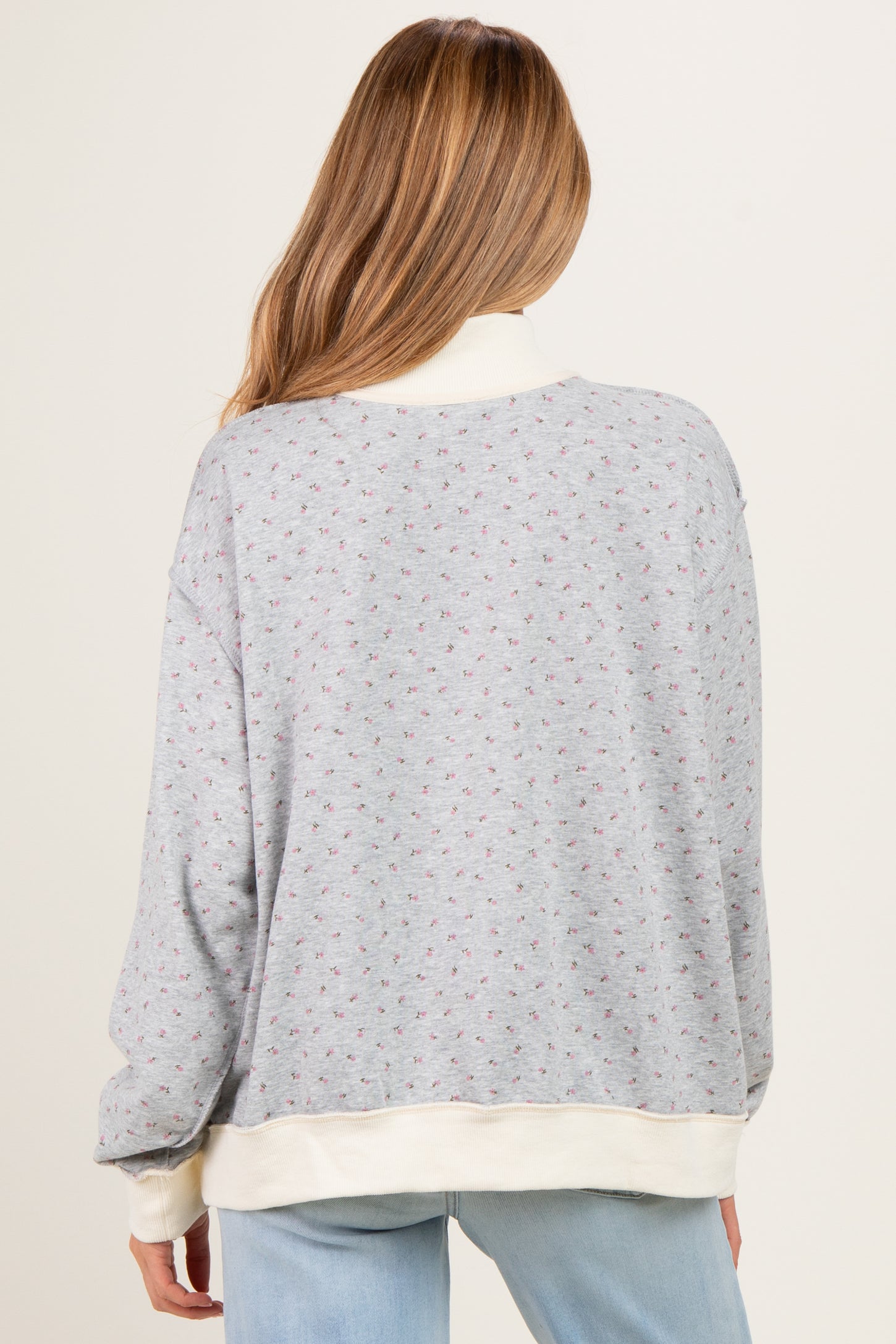 woman wearing a light gray maternity sweatshirt with a floral pattern and cream-colored trim, viewed from the back