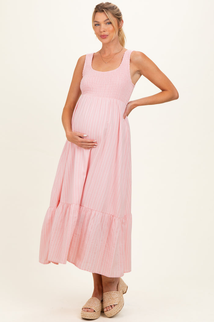 woman wearing a light pink striped maternity maxi dress with smocked bodice and ruffled hem, showing her baby bump