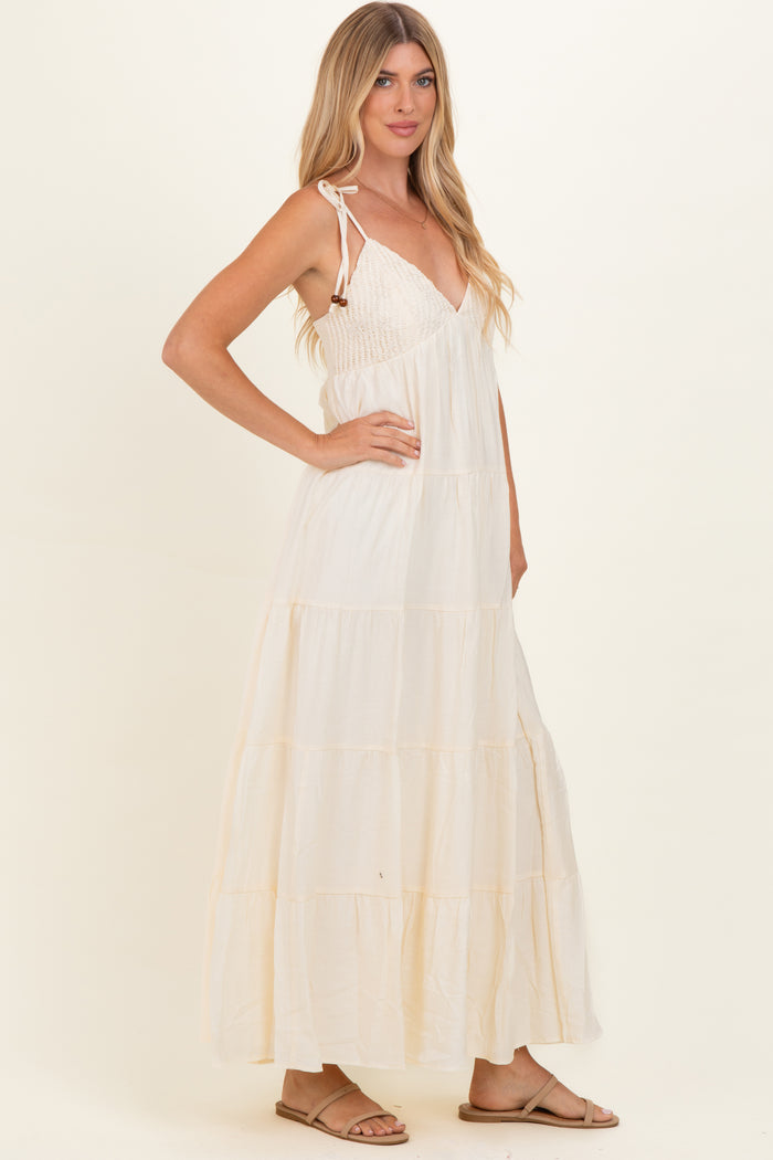 woman wearing a cream colored maxi dress with tie straps and tiered skirt, standing in profile with a relaxed pose