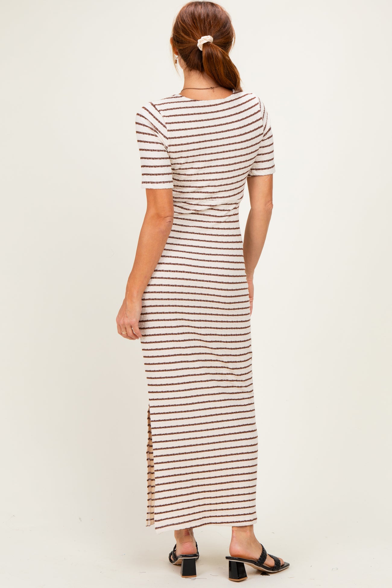 woman wearing a striped midi dress with short sleeves and side slits, styled with black sandals