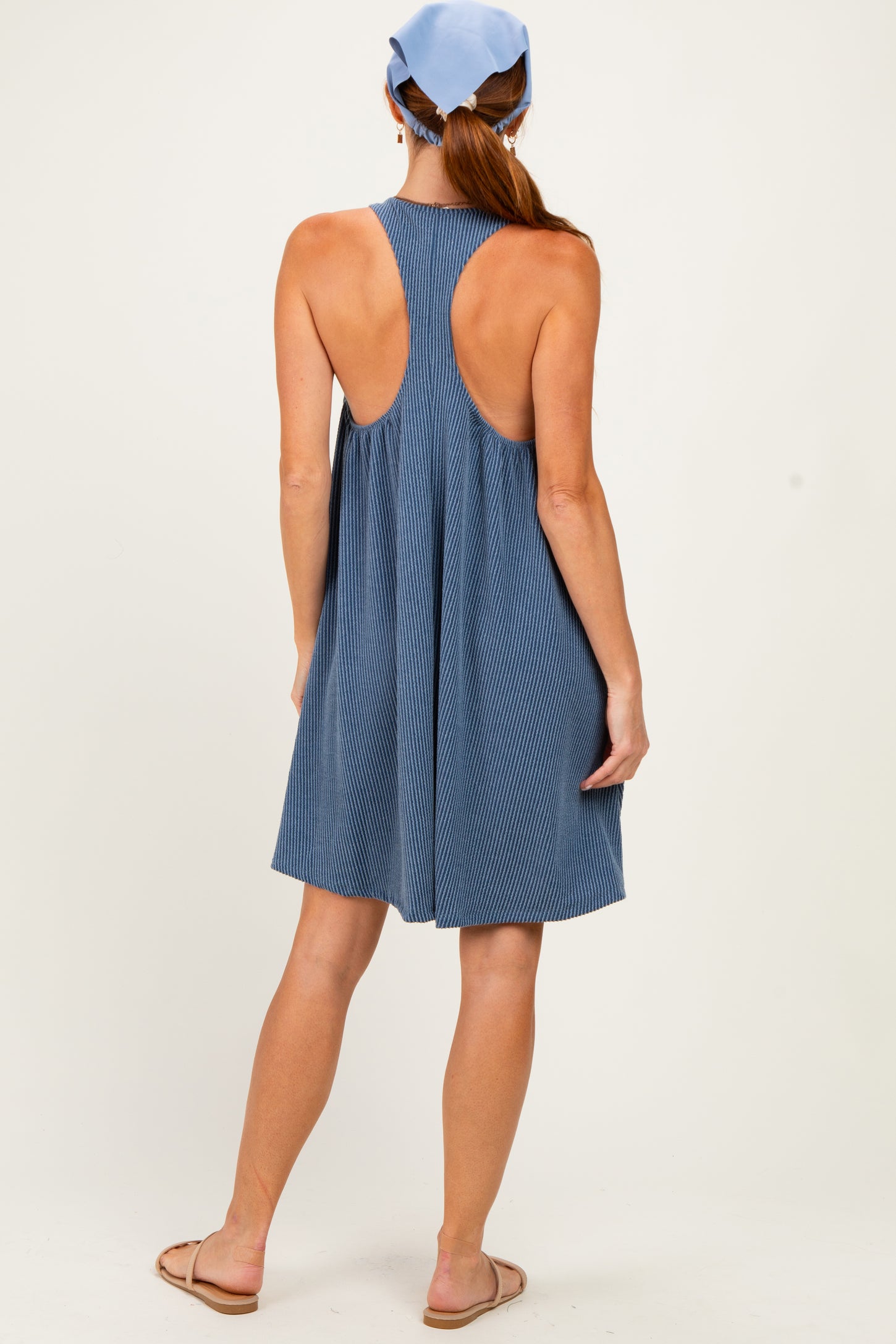 woman wearing a blue striped sleeveless dress with an open back, styled with a light blue headscarf