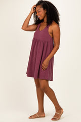 woman wearing a maroon striped sleeveless dress with a flowy skirt and sandals, smiling while touching her hair