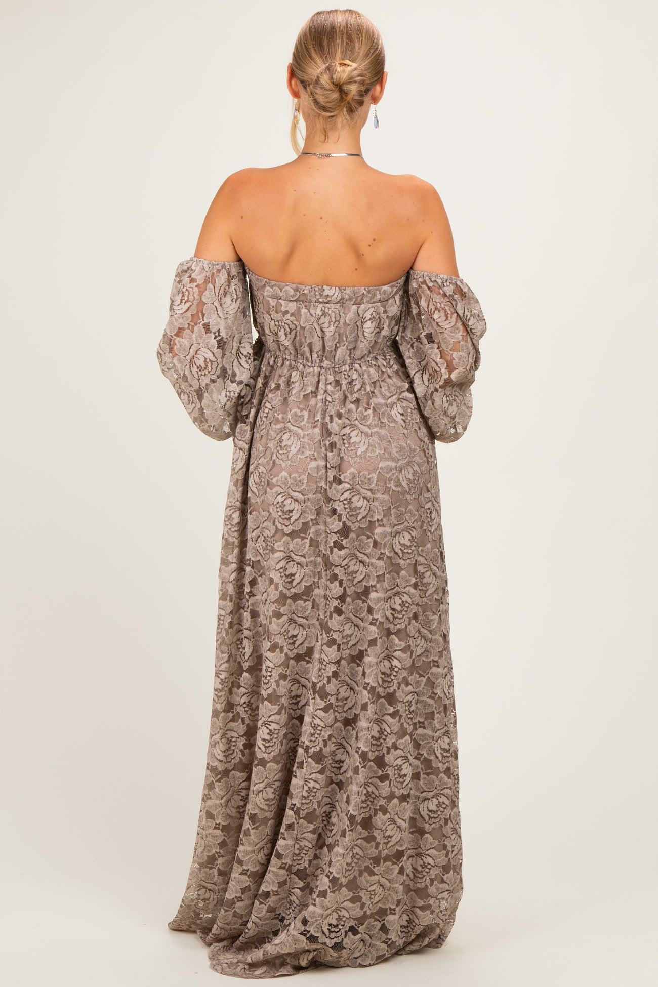 woman wearing a back view of a long, off-the-shoulder lace maxi dress in a muted taupe color