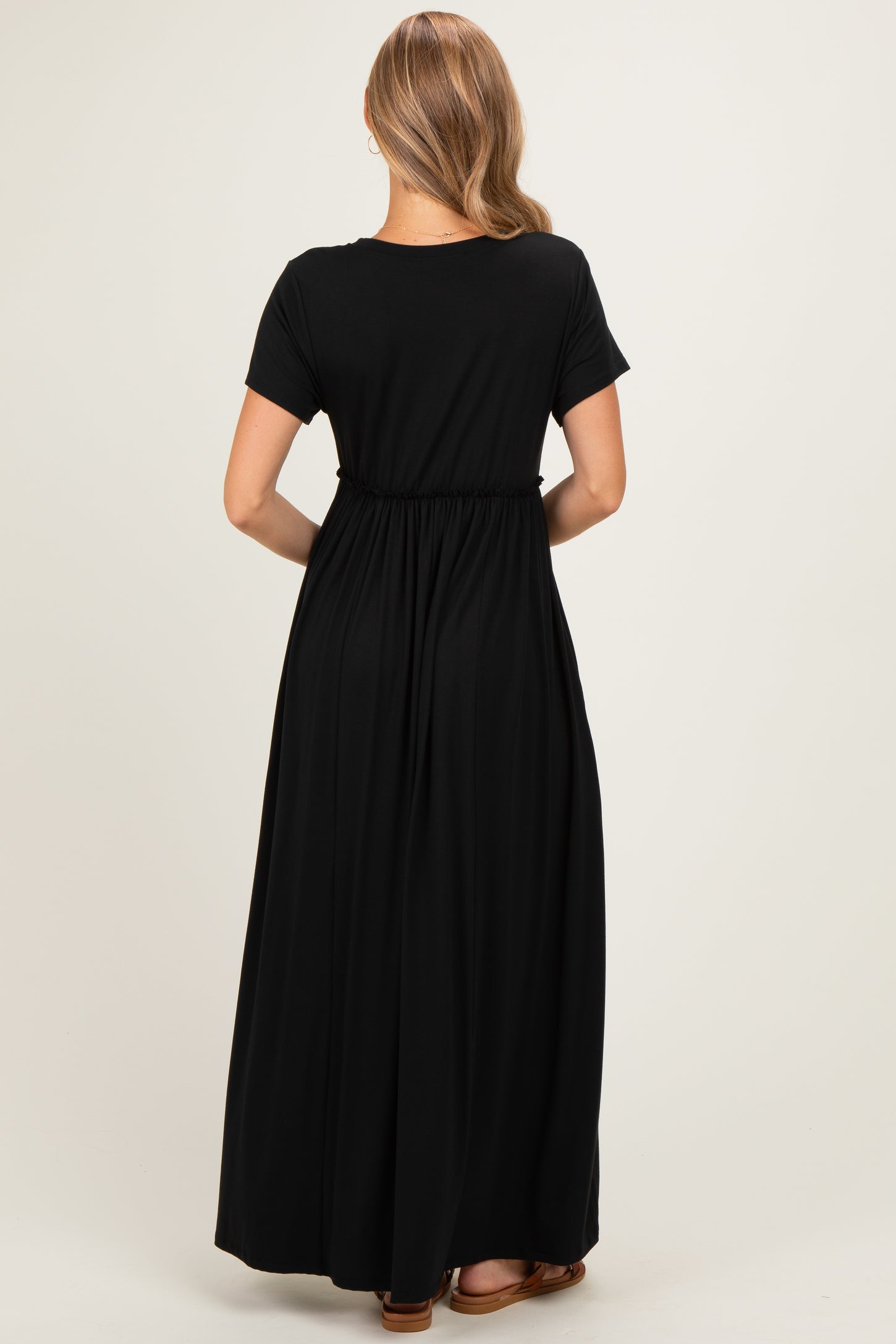 woman wearing a black maxi dress with a gathered waist and short sleeves, shown from the back
