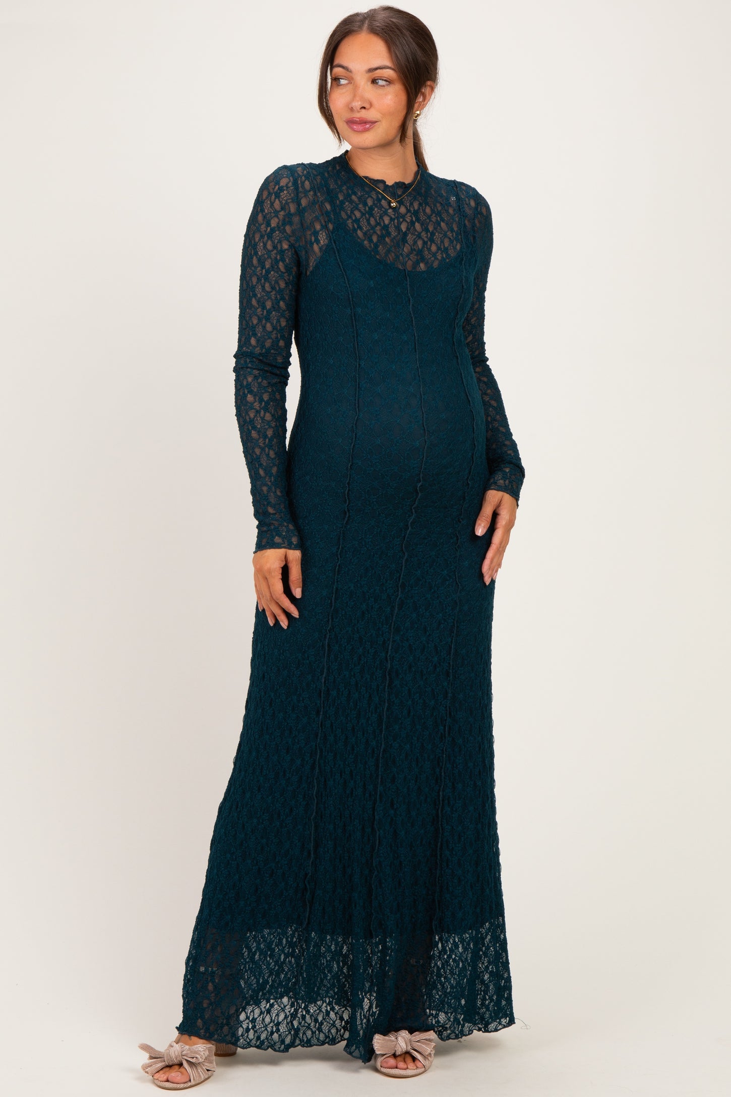 woman wearing a teal lace maternity maxi dress with long sleeves and a fitted silhouette, showcasing her baby bump
