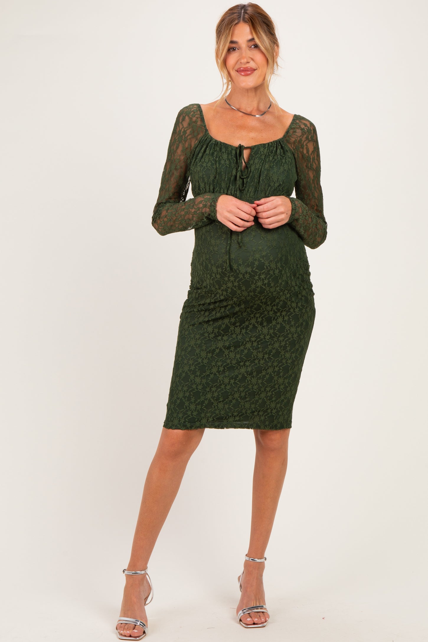 woman wearing a dark green lace maternity dress with long sleeves and a keyhole neckline, showing her baby bump
